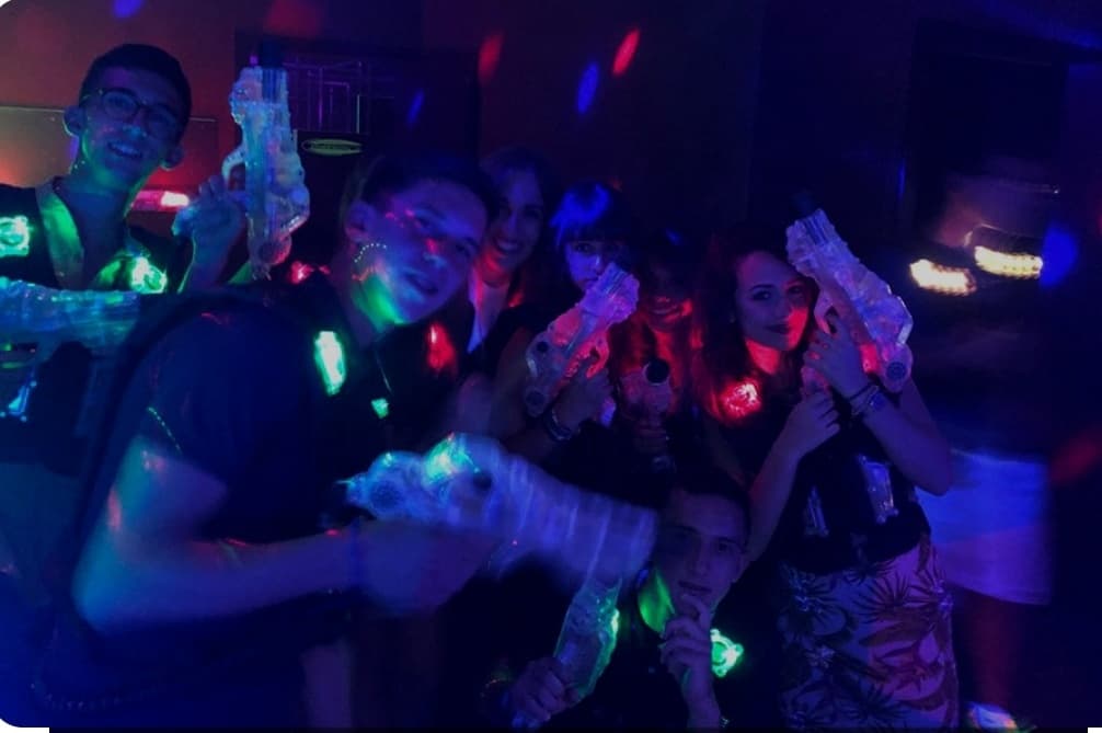 Group playing laser tag in neon-lit indoor arena with foam guns