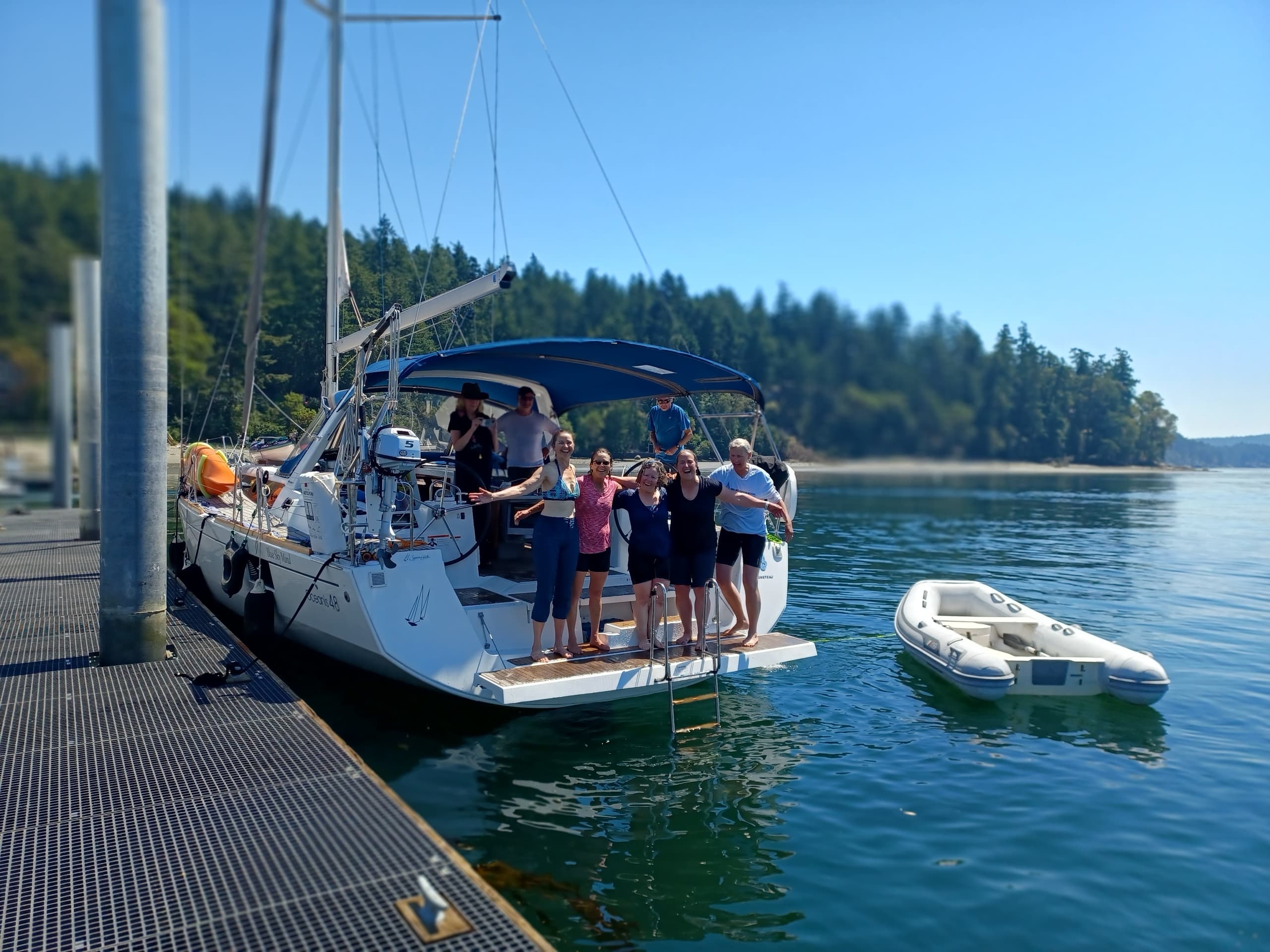 Crew boarding sailboat at marina, scenic forested shoreline