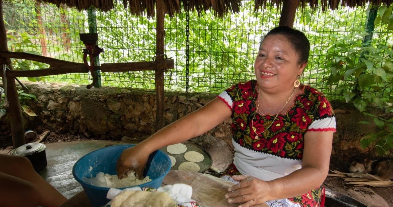 Local cook making corn tortillas under shaded palapa outdoors