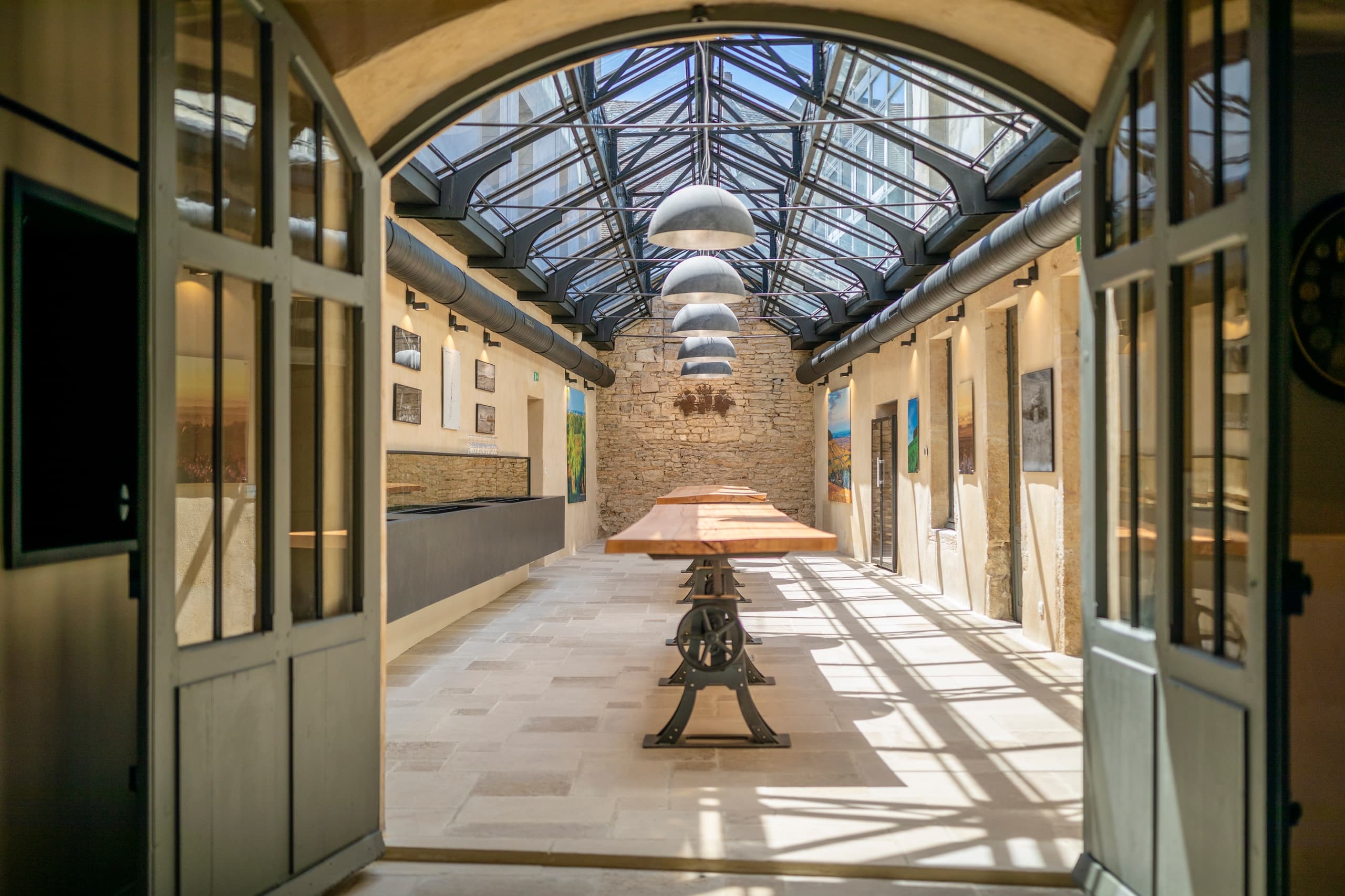 Sunlit glass-roof corridor leading to tasting area with long table