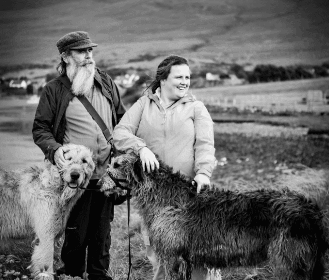 Couple with Irish wolfhounds posing on rural seaside pasture
