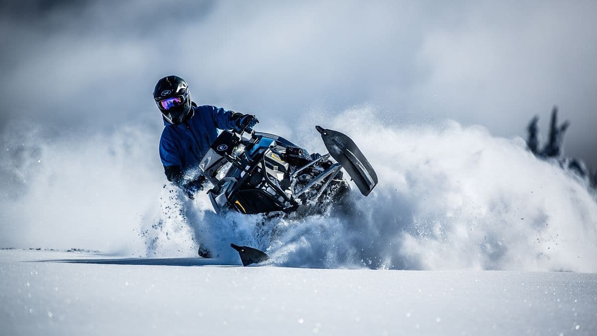 Snowmobiler carving deep powder on backcountry snowy slope