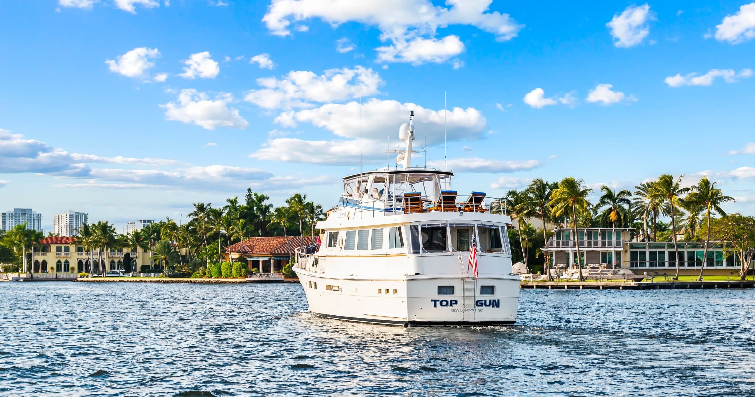 Motor yacht cruising bayfront past palms and waterfront homes