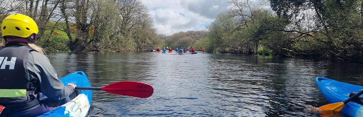 Kayakers paddling along tree-lined river, calm scenic touring