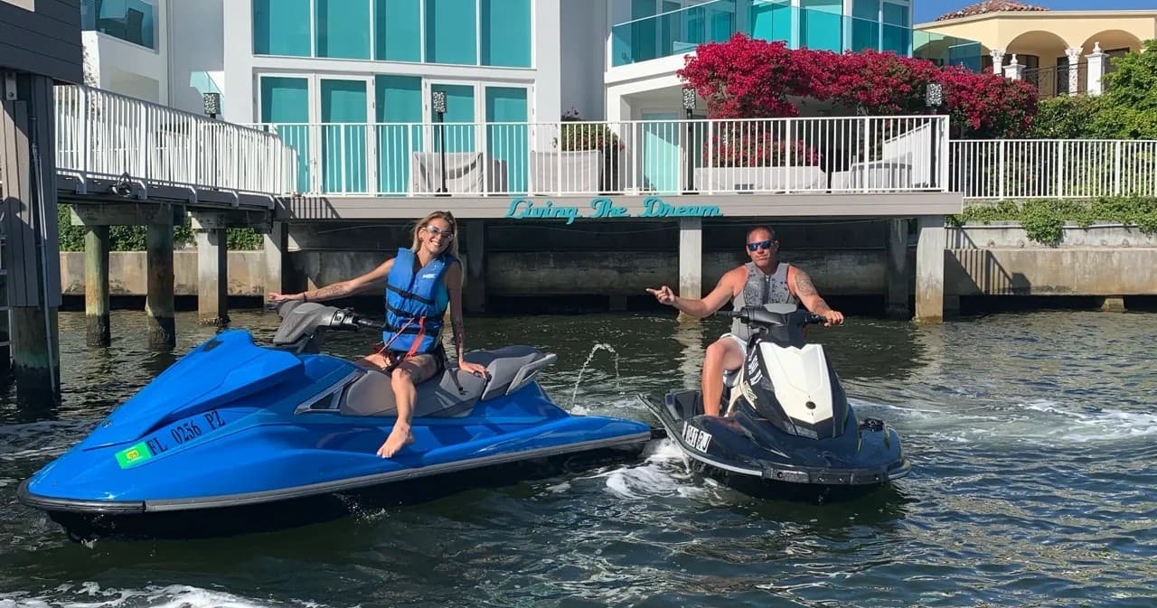 Two riders jet skiing near waterfront homes on sunny bay