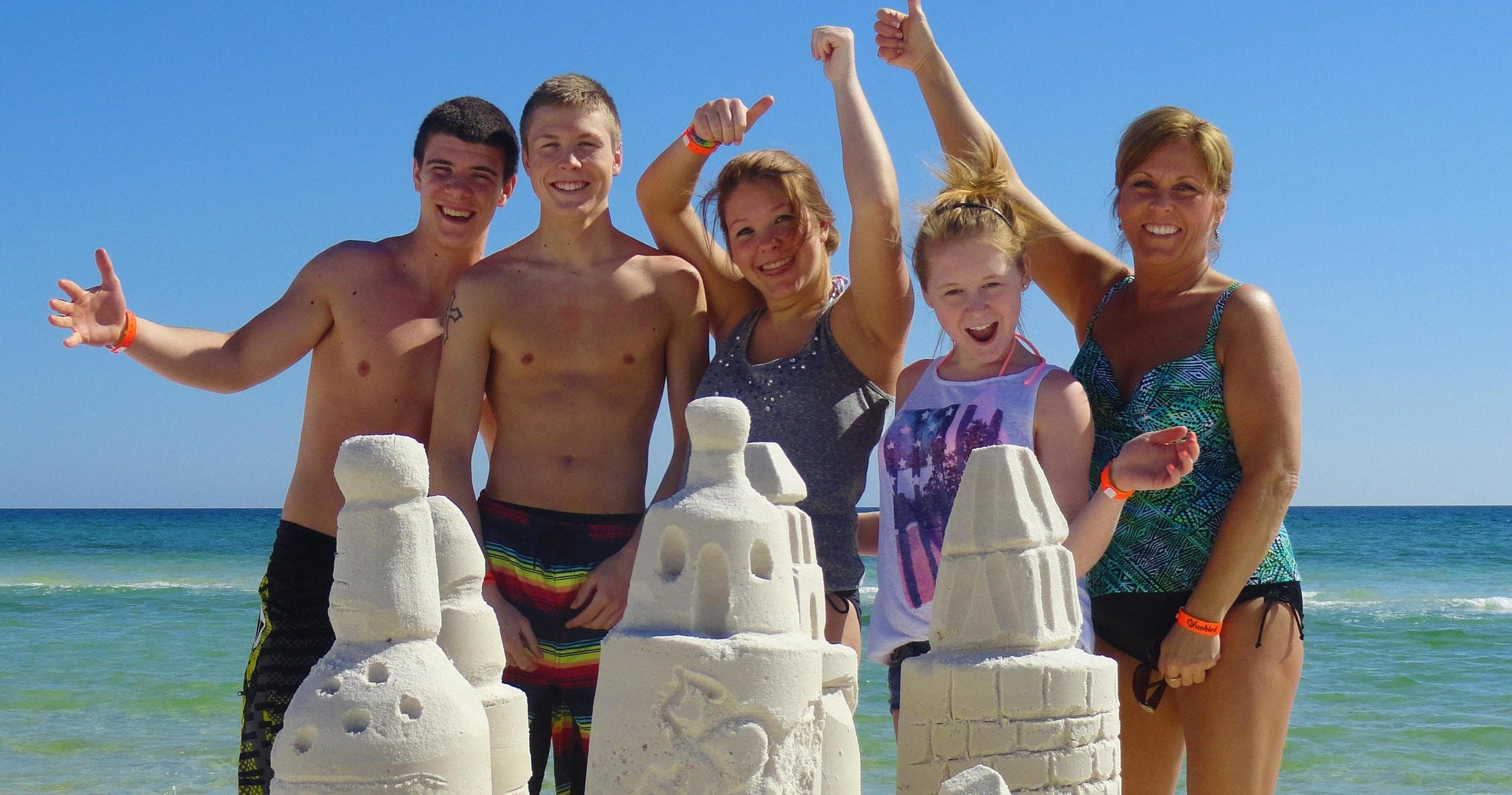 Friends cheering behind sand sculptures on Gulf Coast beach