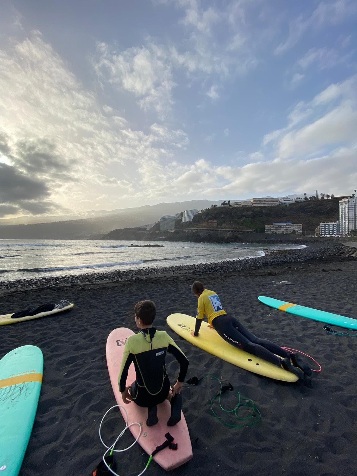 Surfers prepping pastel boards on black sand beach at dusk