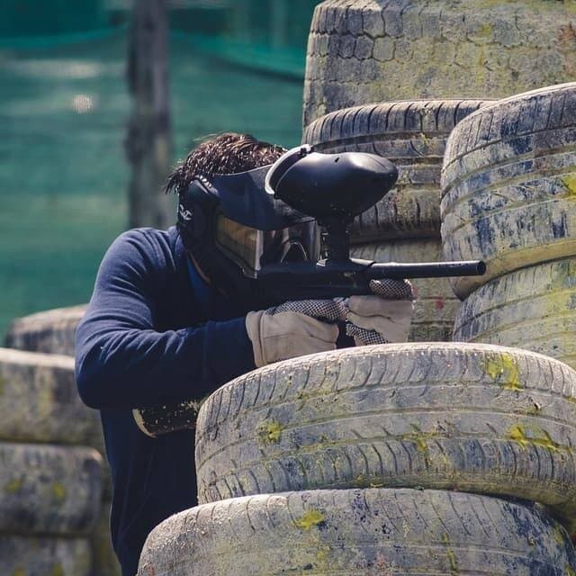 Paintball player taking aim behind tire barricades on course