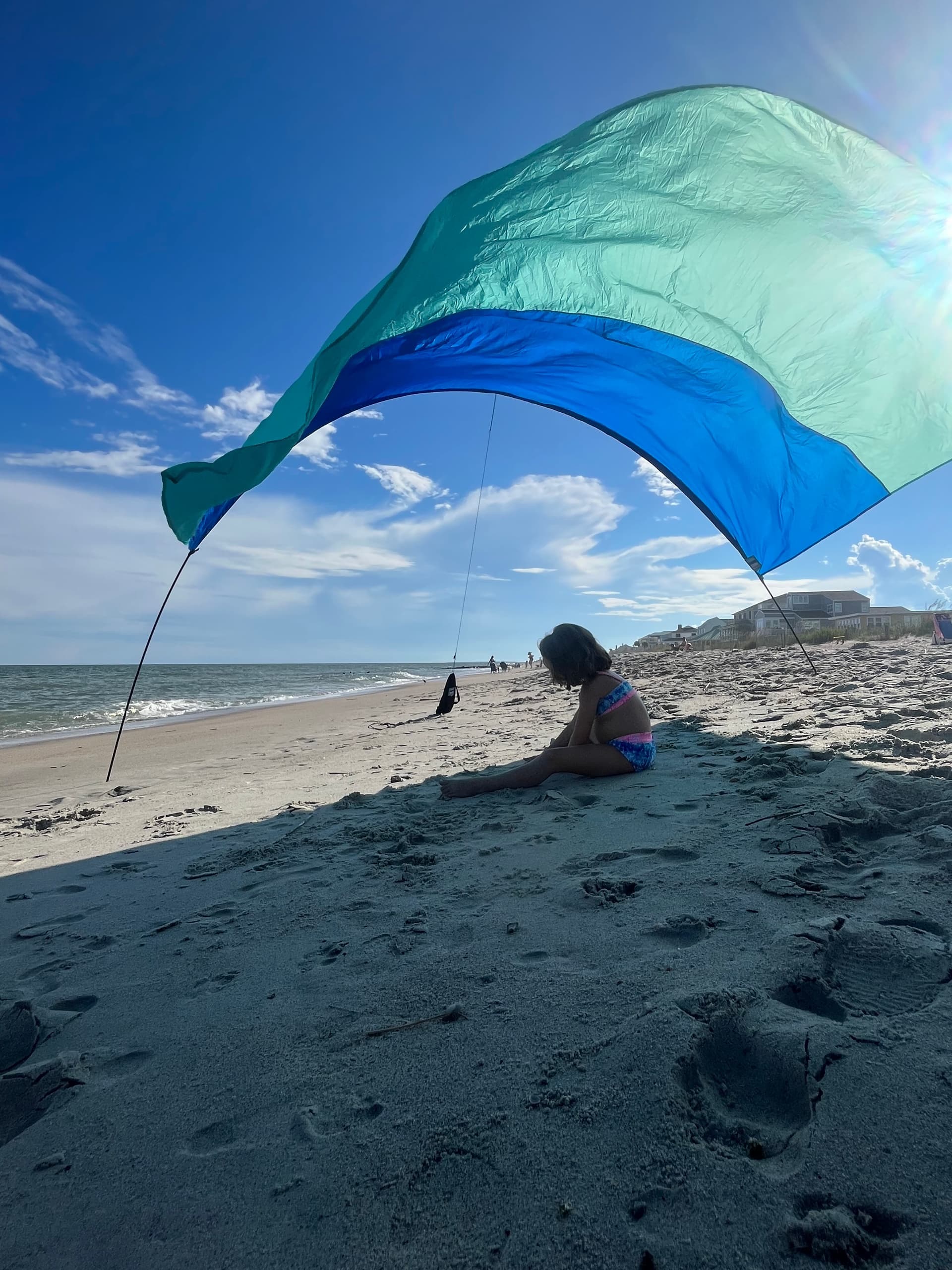 Large blue beach canopy shading child on sandy shore