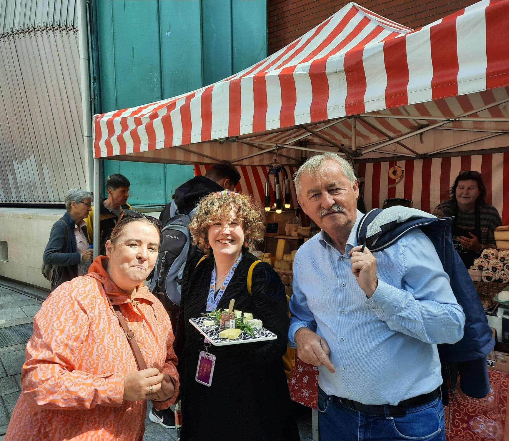 Visitors sampling street food at outdoor market with striped stall