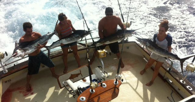 Anglers holding large pelagic fish on choppy ocean-facing deck
