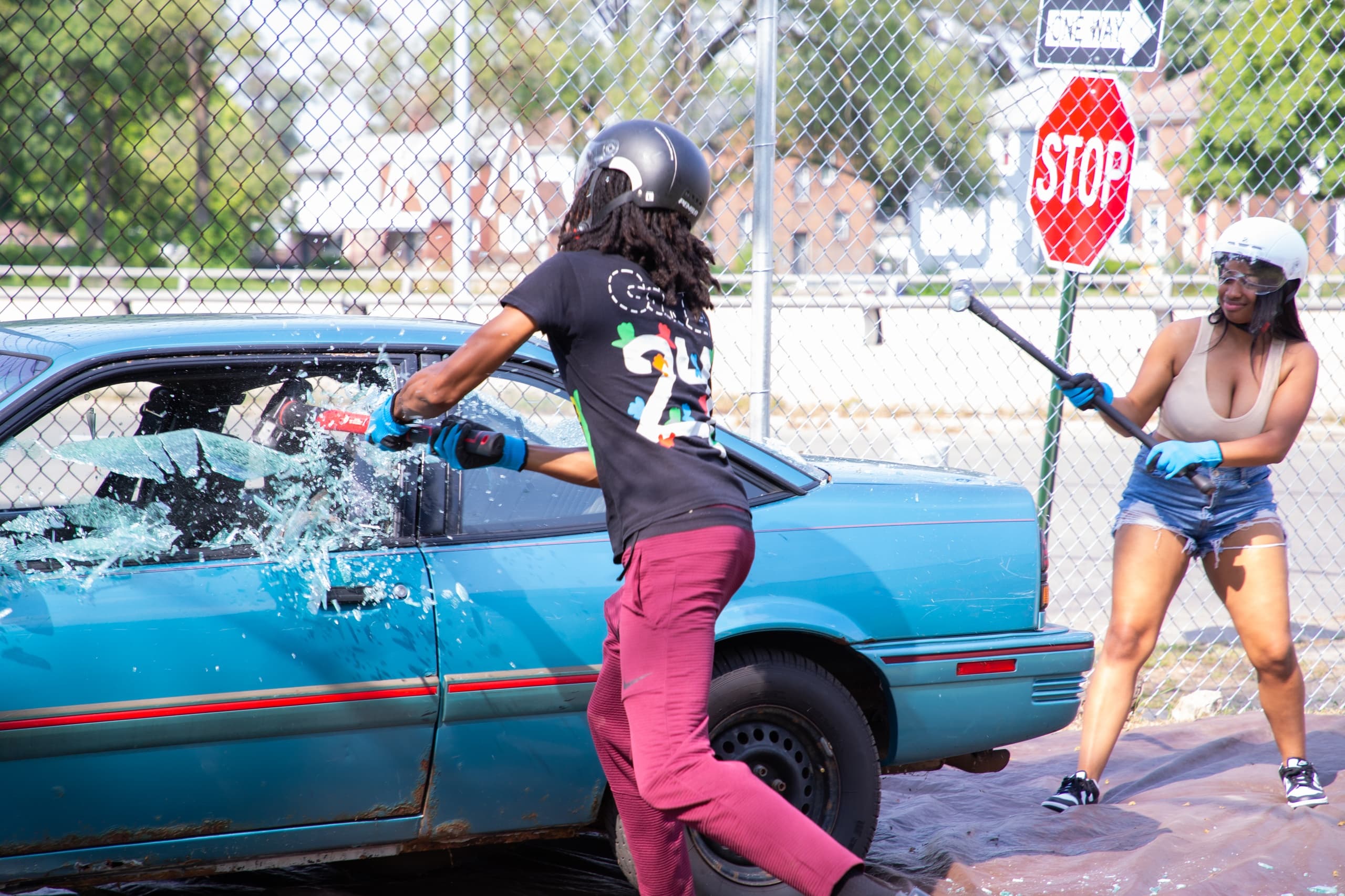 People smashing car at outdoor rage event by chainlink fence