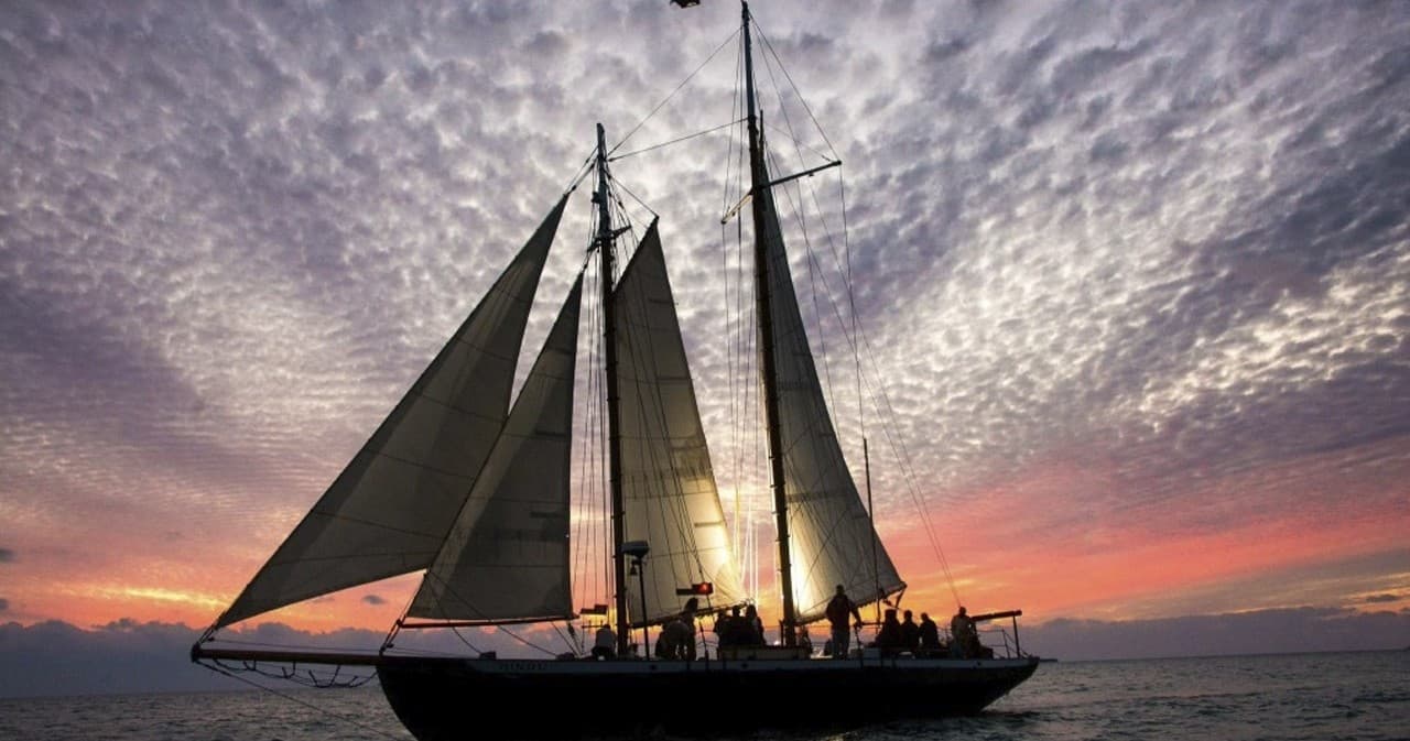 Tall schooner sailing at sunset over calm ocean waters