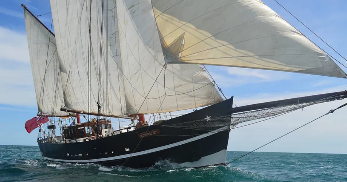 Tall ship under full sail cutting through turquoise open sea