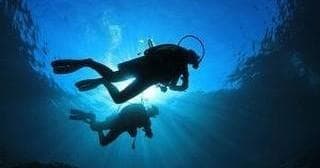 Silhouetted scuba divers ascending with sunburst over ocean