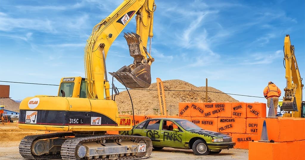 Compact track loader scooping dirt next to orange barriers outdoors