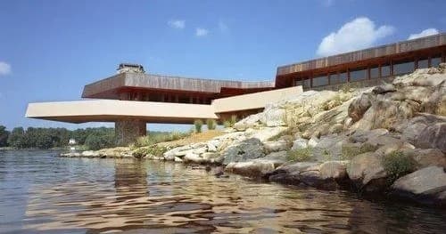 Viewing modern cantilevered building over rocky lakeshore, waterfront vista