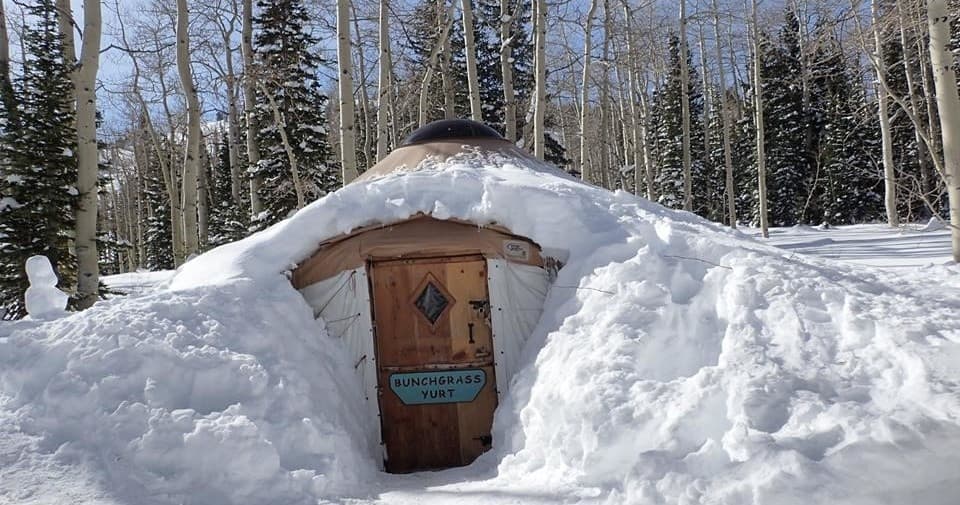 Snow-buried hut entrance in aspen forest for ski hut stay