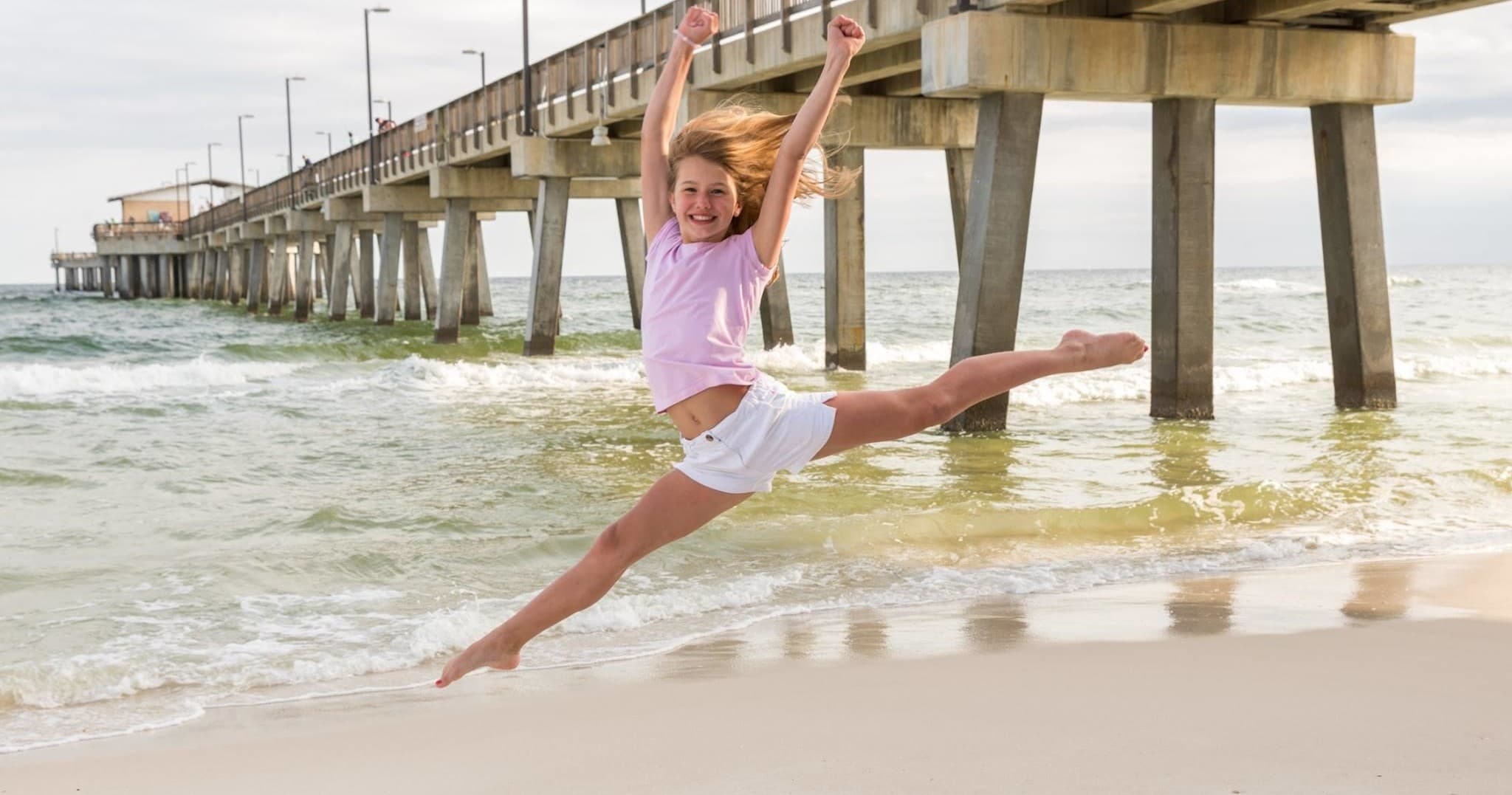 Dancer leaping on shoreline under pier at Orange Beach
