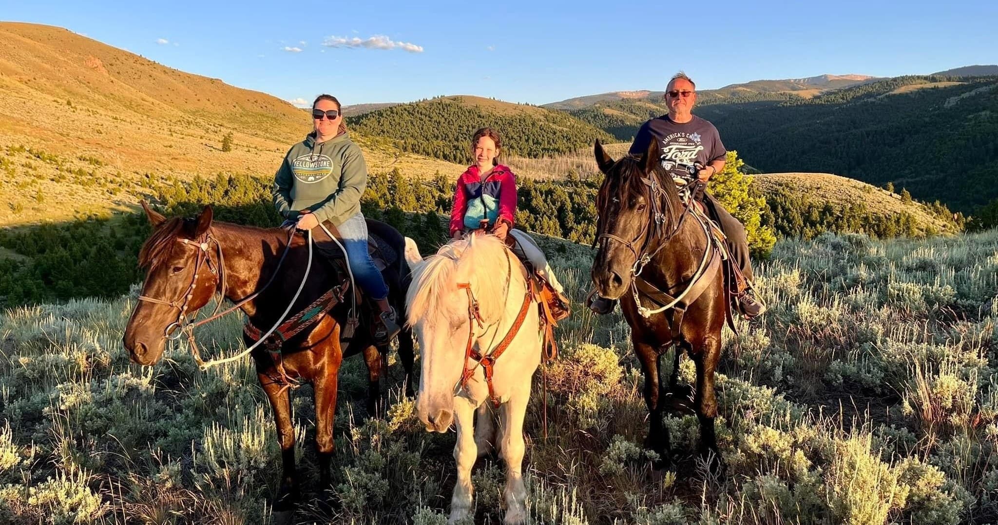 Three riders horseback riding through golden mountain foothills