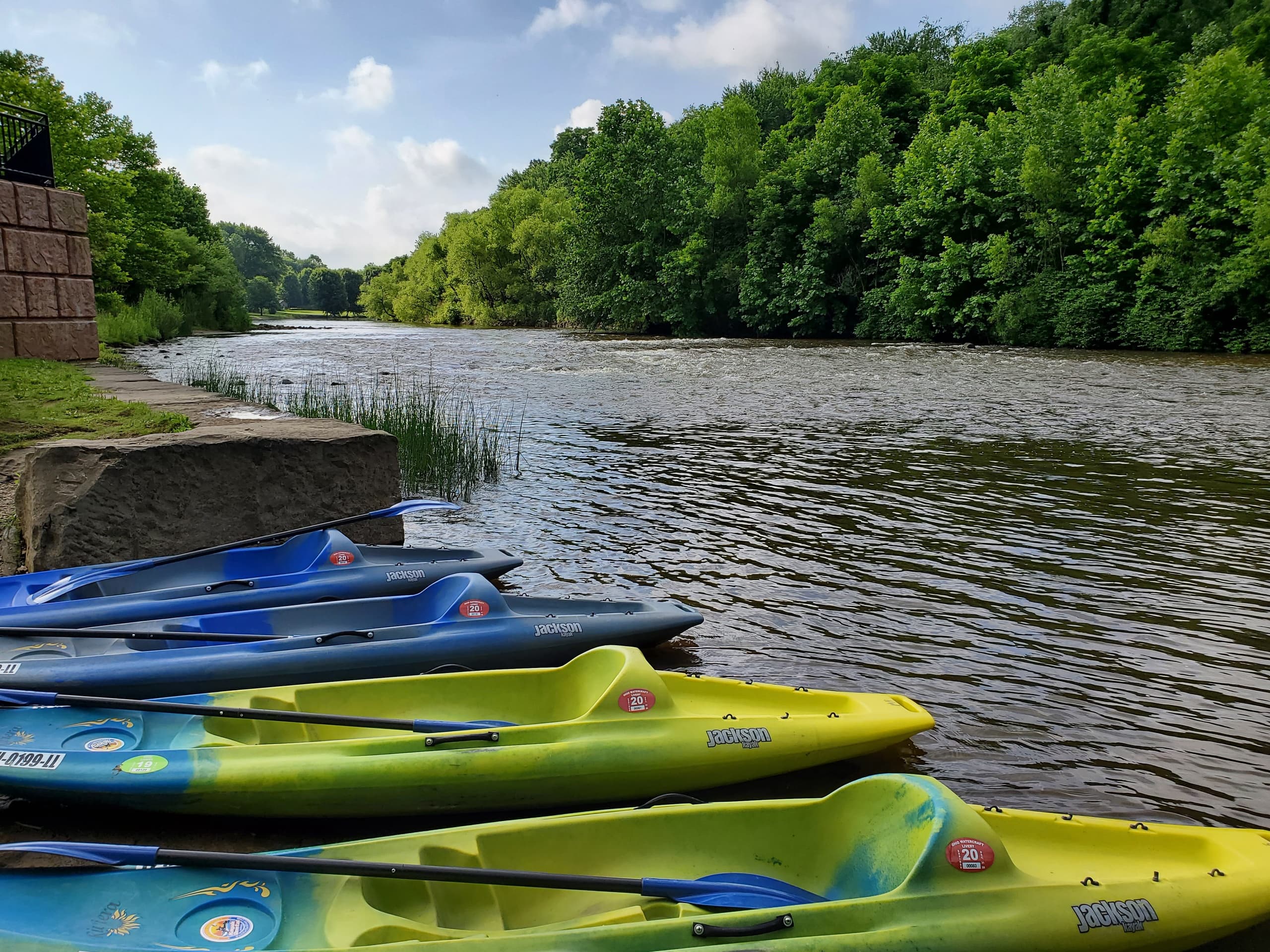 Stacked bright kayaks on riverbank for rental and tours