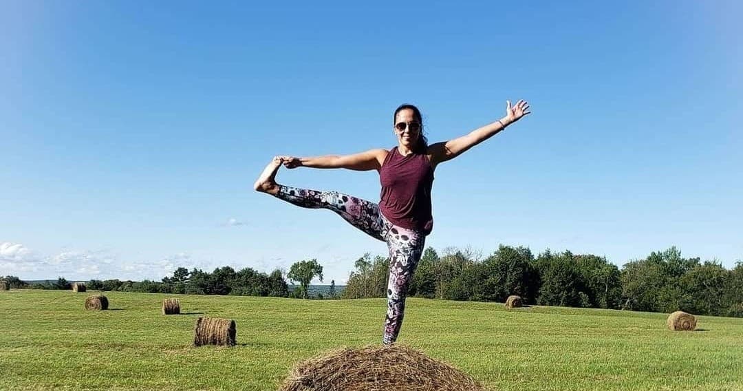 Person practicing yoga on hay bale in open abmasfarm meadow