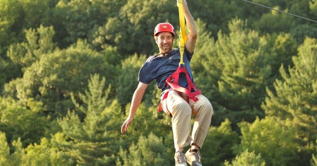 Thrill-seeker ziplining over dense green forest at Berkshire resort