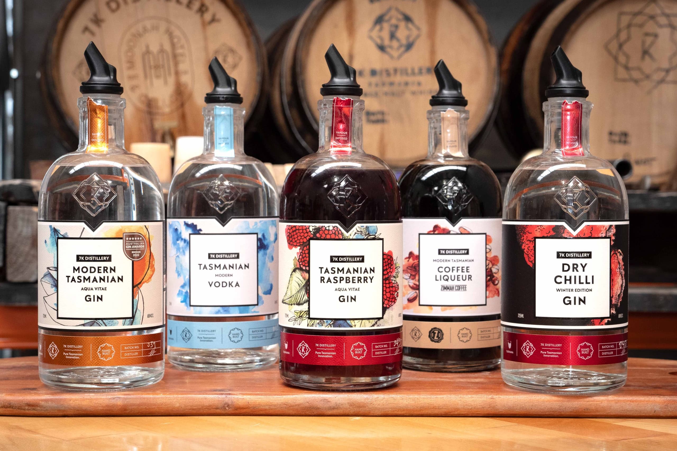 Bottles of craft spirits lined on wooden bar in distillery with oak barrels