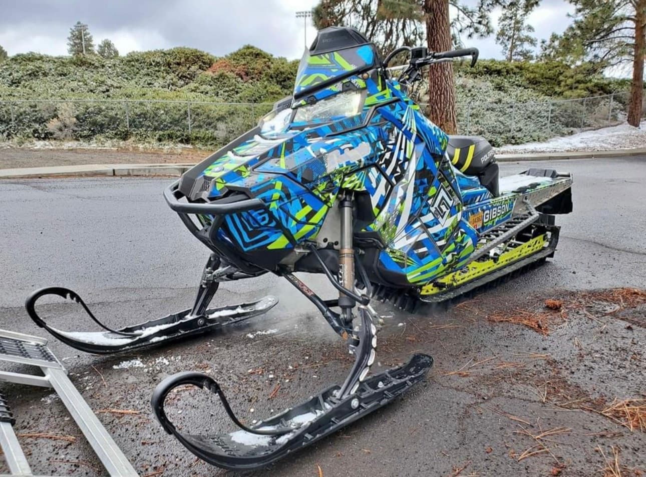 Bright wrapped snowmobile on roadside with pine backdrop