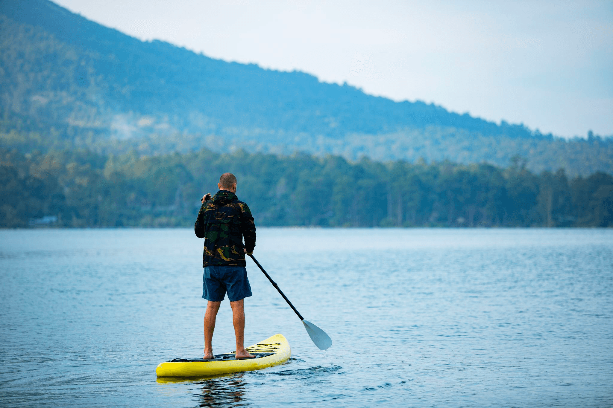 Stand-up paddleboarder on calm mountain lake at sunrise