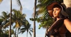 Woman wearing hat by palm trees on sunlit tropical beach