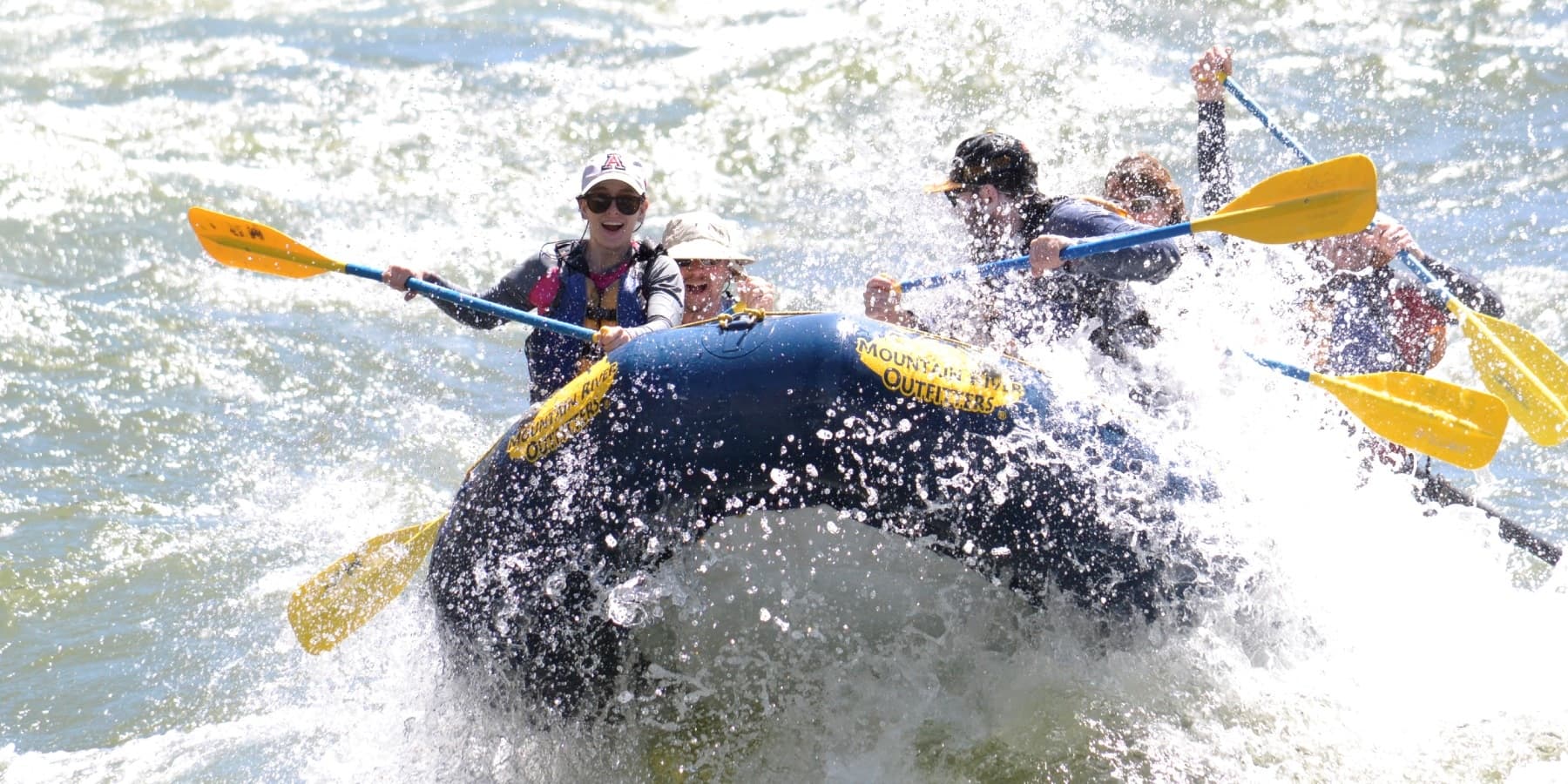 Rafting crew bursting through big wave on turbulent river rapids