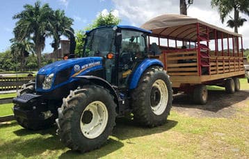 Blue tractor hitched to covered hayride wagon on rainforest field
