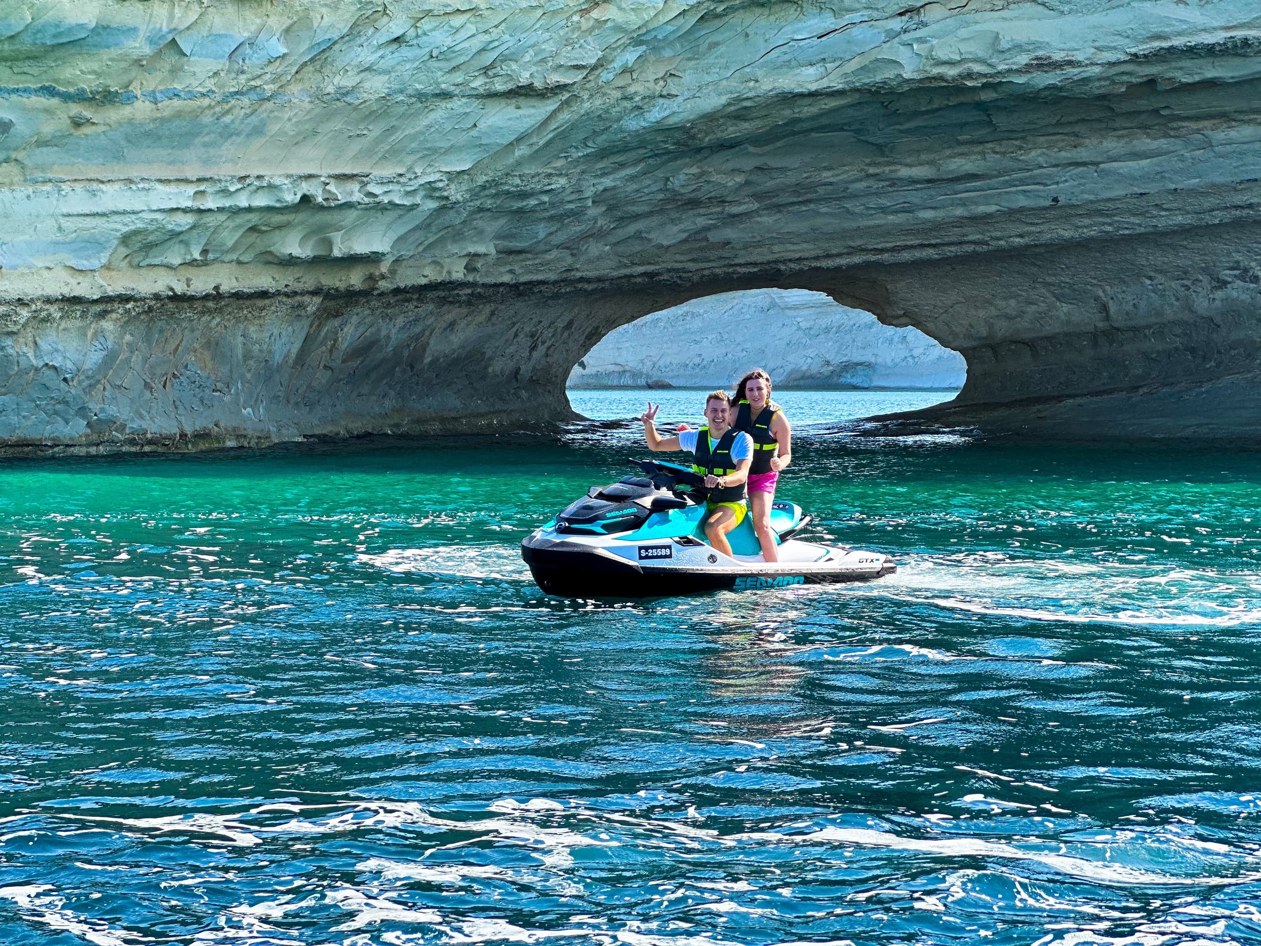 Jet ski riders speeding under sea arch in turquoise coastal waters
