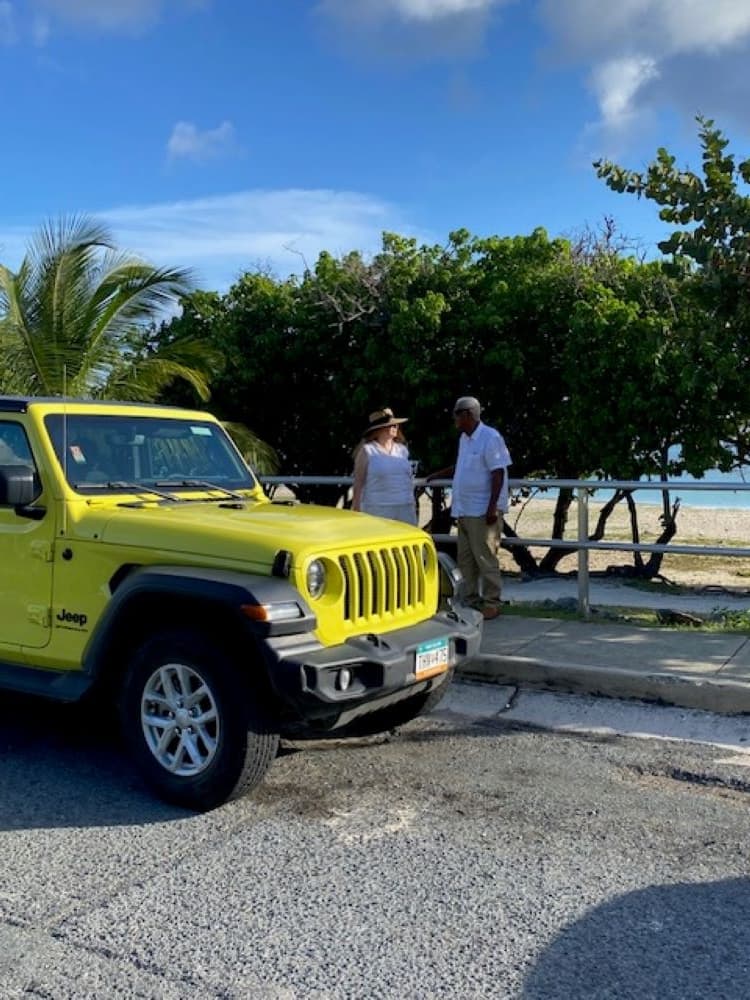 Bright yellow Jeep parked near sandy beach and palm trees