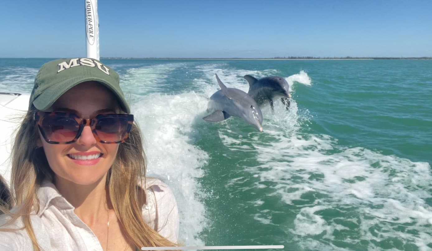 Angler selfie with dolphins riding wake, nearshore boating adventure