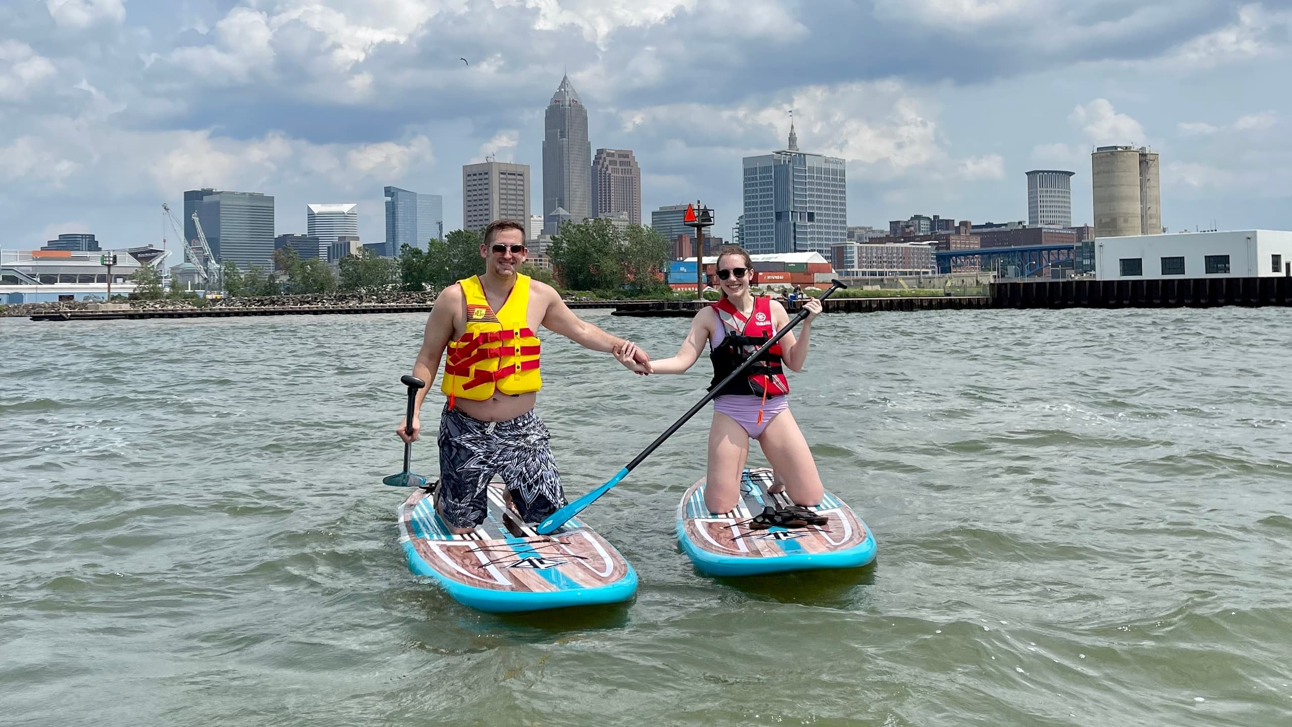 Couple paddleboarding on river with city skyline backdrop