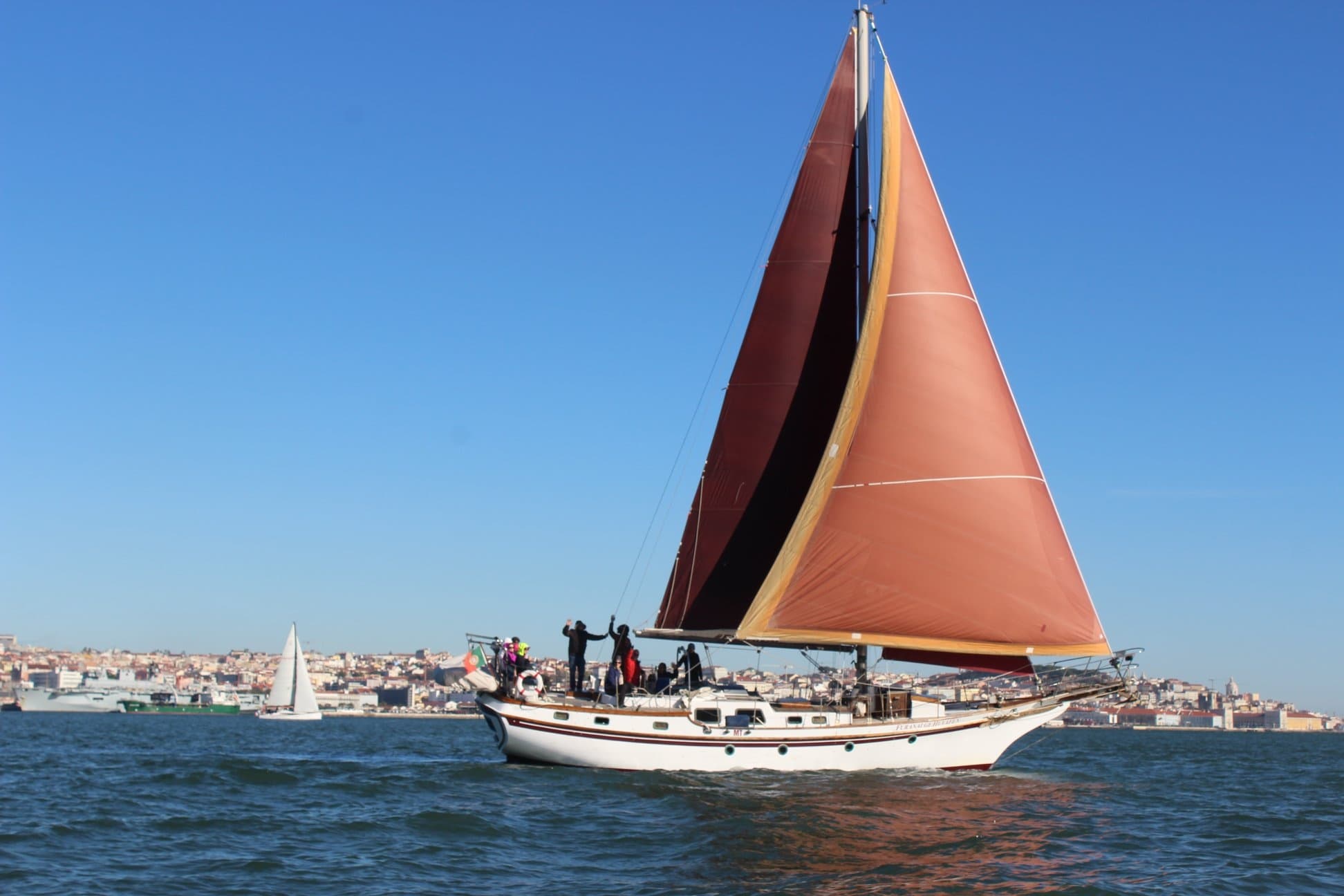 Sailboat with red sail cruising near coastal city skyline