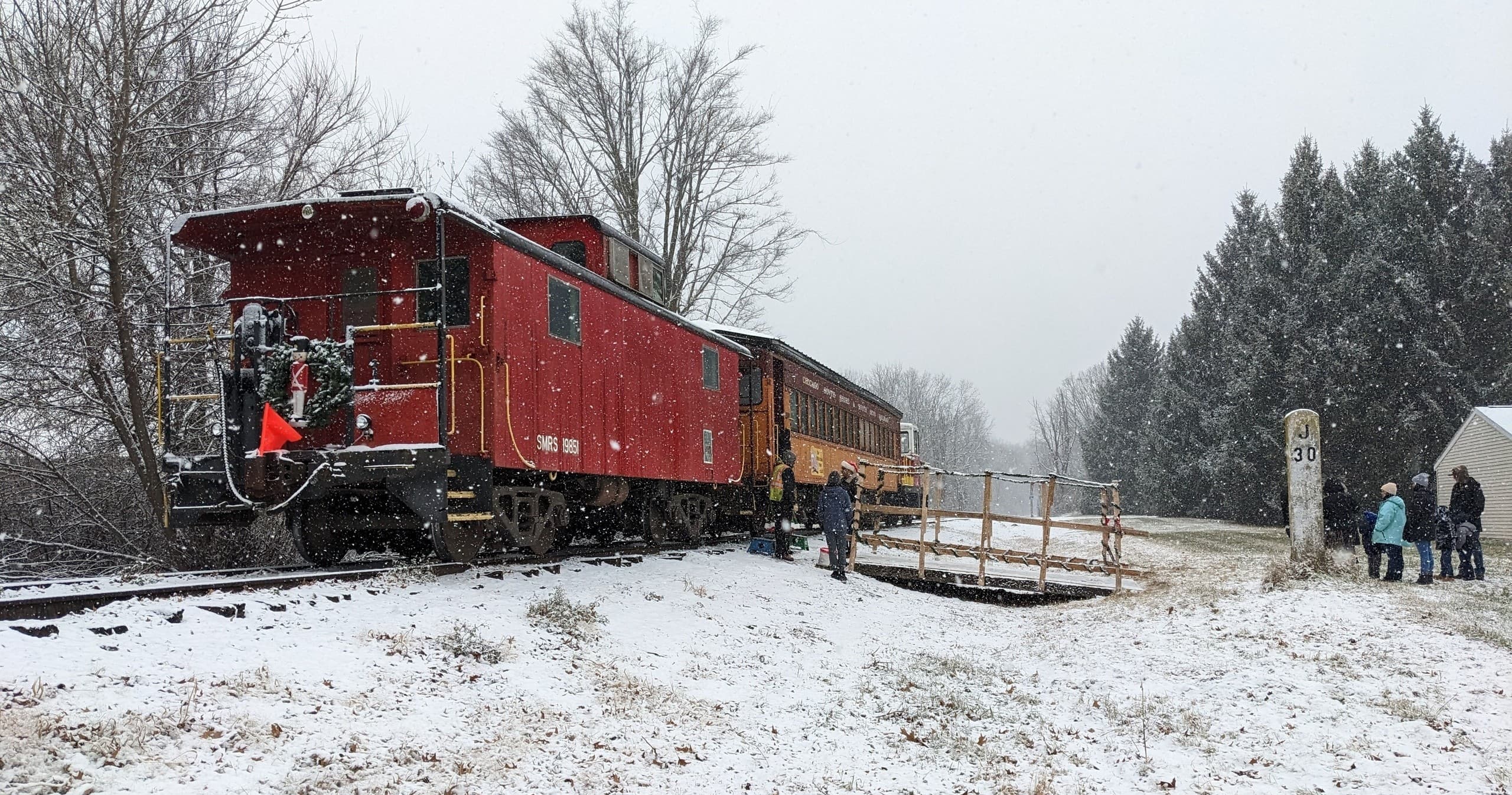 Red caboose on snowy rural tracks with passengers boarding