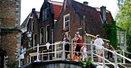 Tourists on narrow historic canal bridge sightseeing in Dutch town