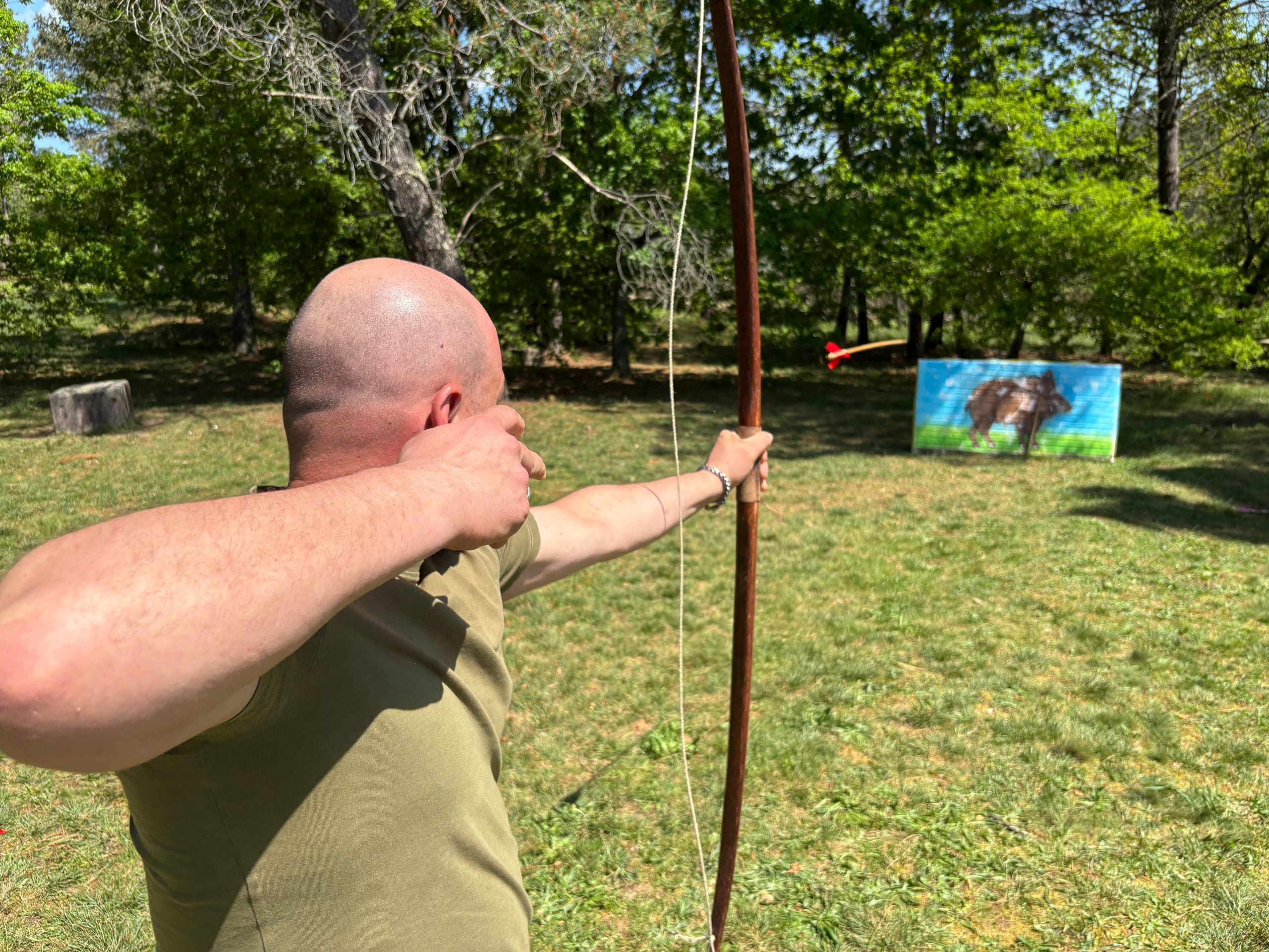 Archer aiming a longbow at an outdoor grassy target range
