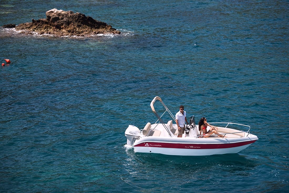 Small motorboat cruising near rocky islet in open Mediterranean sea