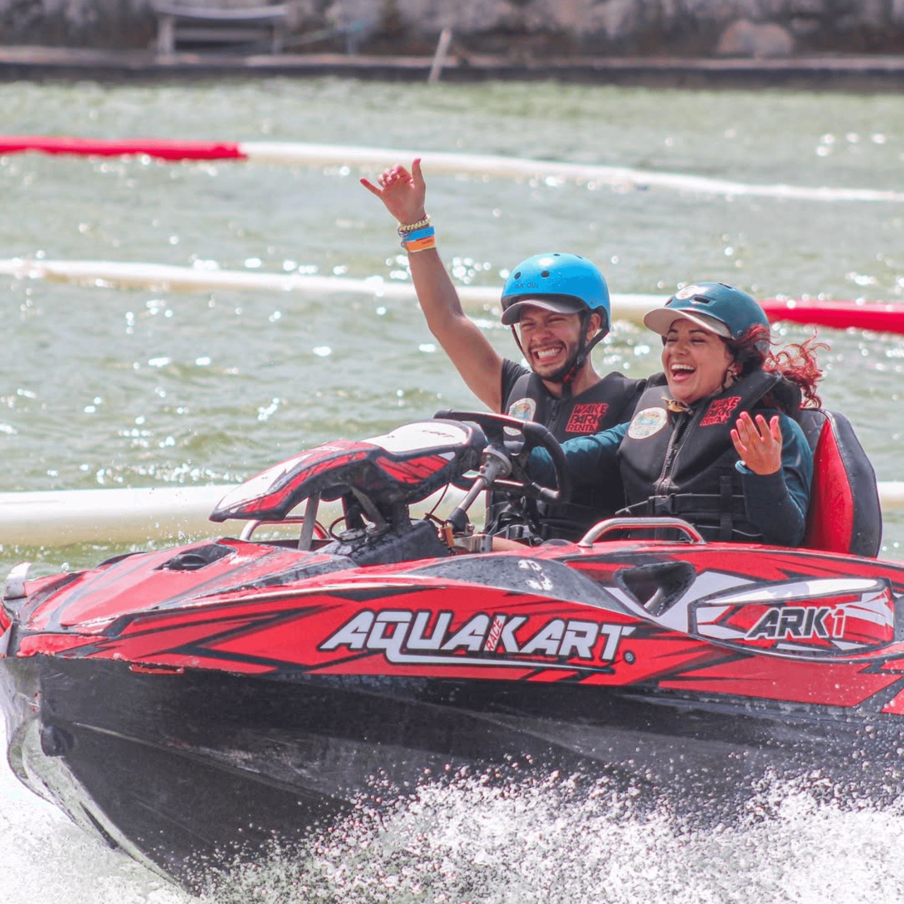 Two riders in red AquaKart racing across clear tropical lagoon