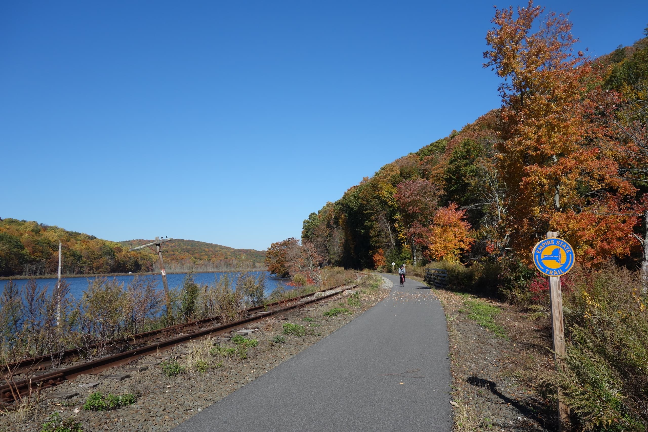 Paved riverside trail beside rail line with distant autumn hills