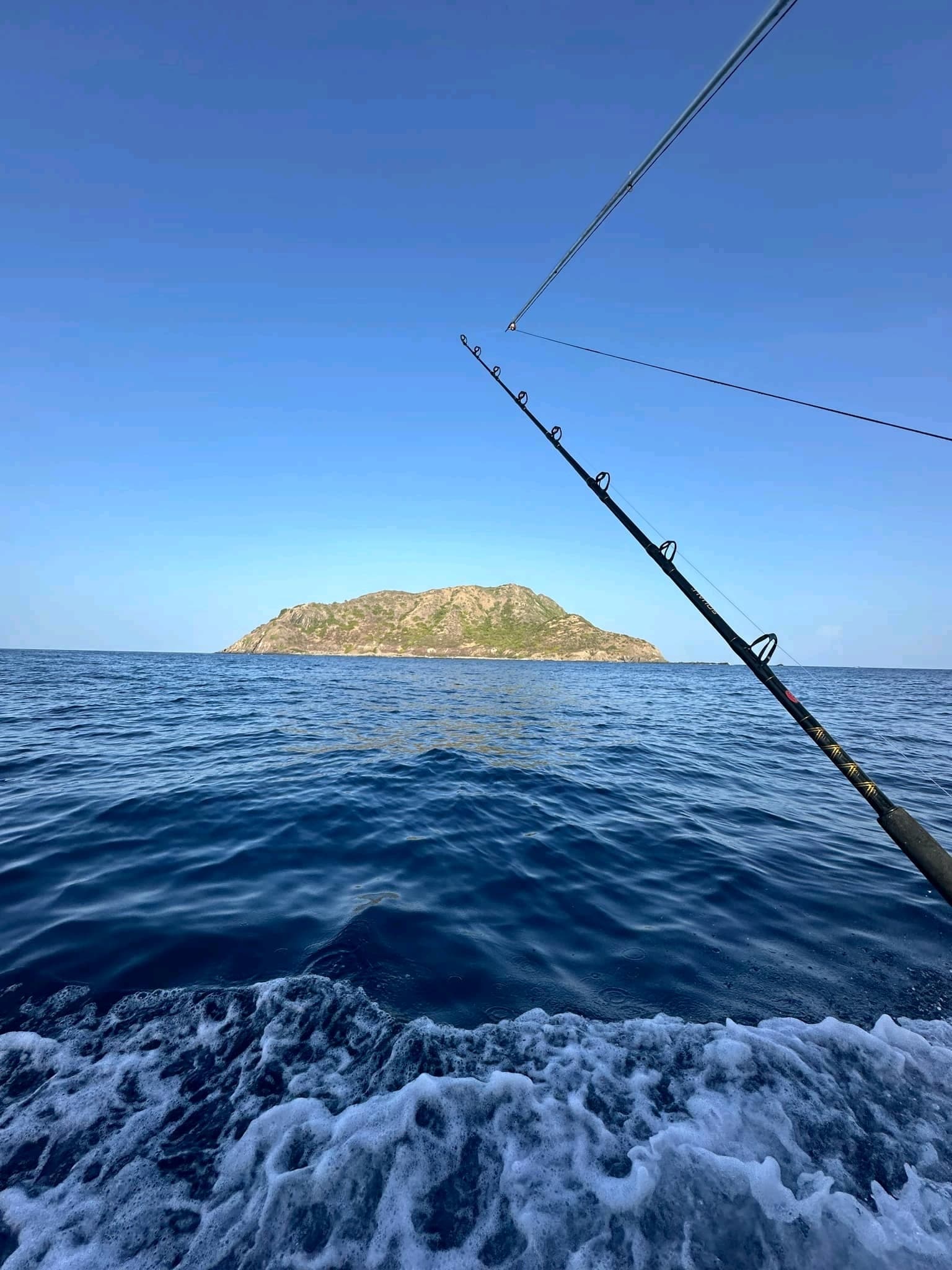 Deep-sea fishing rod over blue ocean toward rocky island vista