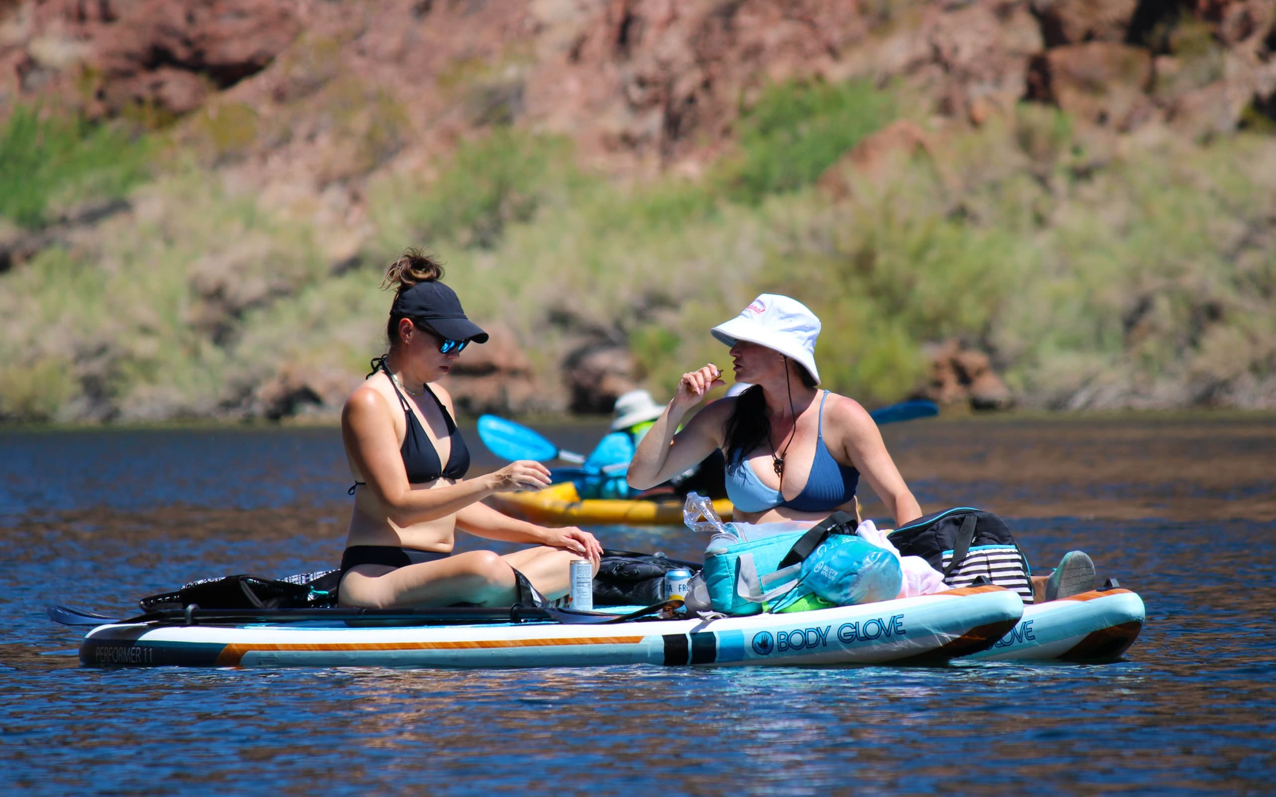 Two paddleboarders socializing on calm river near rocky shore