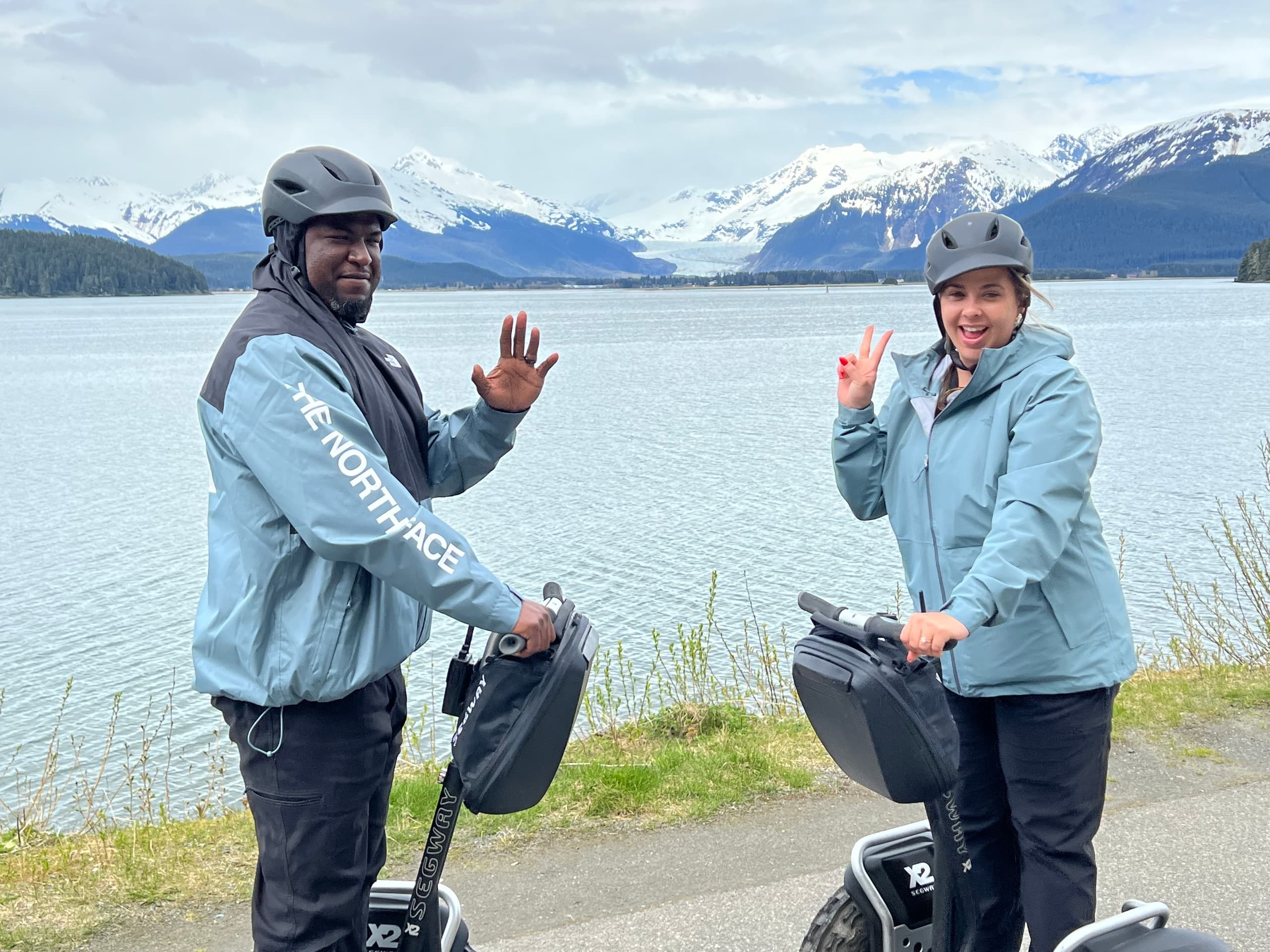 Two guides on Segways waving by glacial lake and mountains