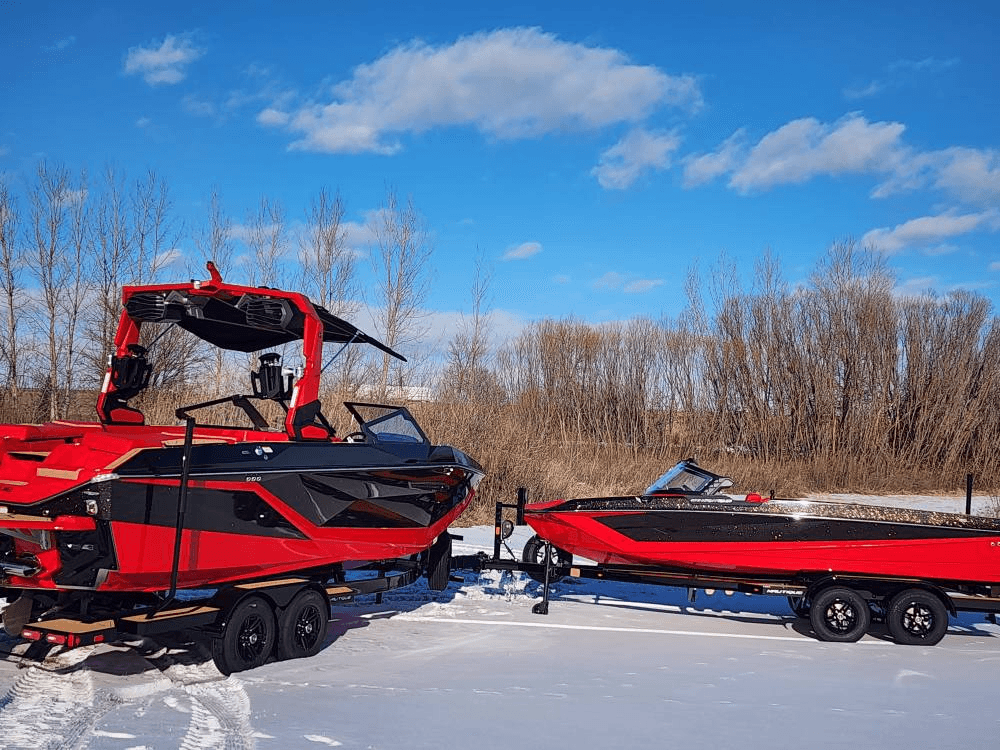 Red wake boats parked on snowy lakeshore trailers