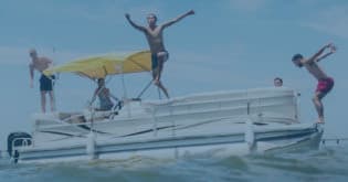 Friends jumping off pontoon boat into coastal bay water