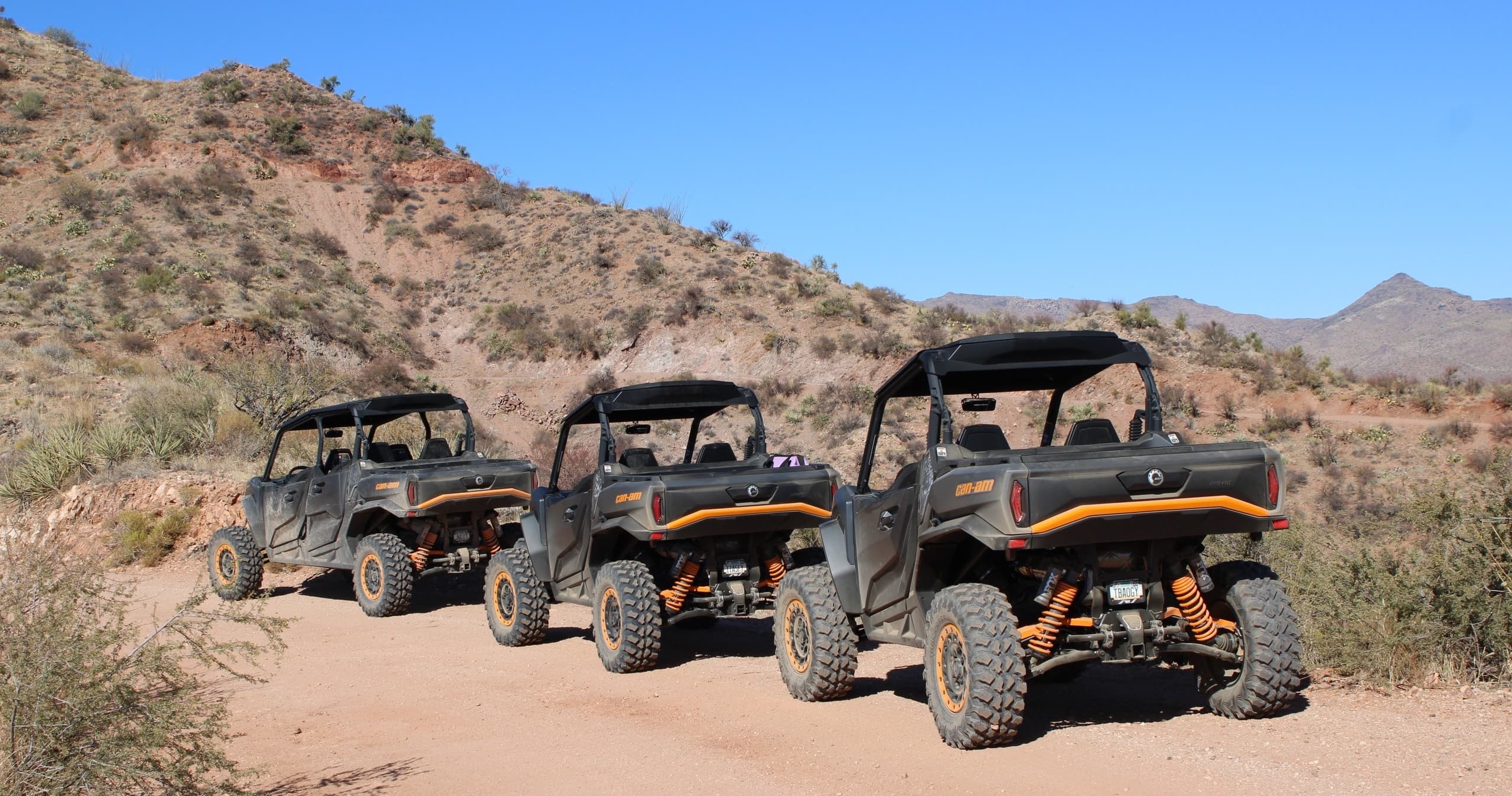 Three UTVs lined up on sandy trail under blue sky in Arizona desert